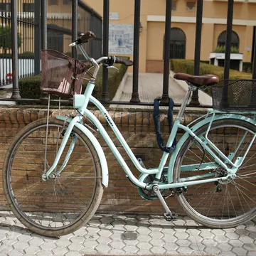 A mint green city bike with a front and a rear basket, leaning on a brick wall