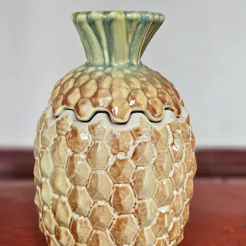 A glazed ceramic jar shaped like a pineapple, with a lid