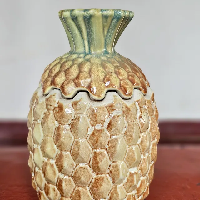 A glazed ceramic jar shaped like a pineapple, with a lid