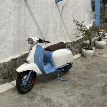 A white and light blue vintage scooter parked against a whitewashed wall