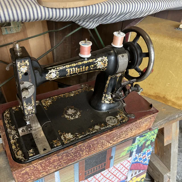 A black antique sewing machine with gold decoration, set in its wooden table
